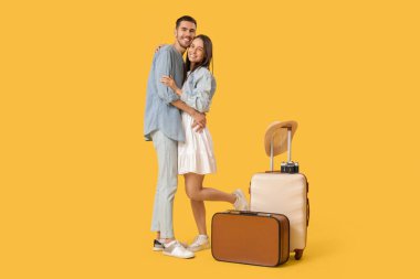 Sarı arka planda bavulları olan güzel, genç, mutlu turistler.