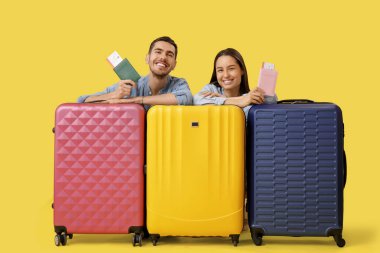 Pasaportları, biletleri ve sarı arka planda bavulları olan mutlu turistler.