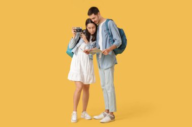 Sırt çantalı, kameralı ve sarı arka planda dünya haritalı güzel mutlu turistler.