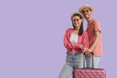 Güzel, genç, mutlu, mor arka planda bavulu olan turistler.