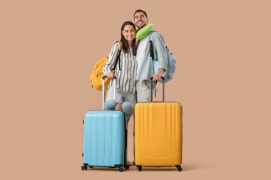 Güzel, genç, mutlu, bavulları, sırt çantaları ve kahverengi arka planda seyahat yastıkları olan turistler.