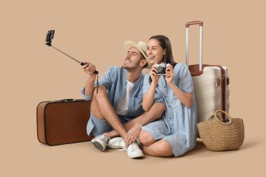 Güzel, genç, mutlu, bavullu ve kameralı turistler kahverengi arka planda selfie çekiyorlar.