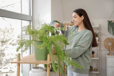 Evdeki çiçekleri sulayan mutlu genç kadın.
