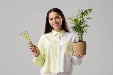 Bahçe tırmığı ve beyaz arka planda bitki yetiştiren genç ve mutlu bir kadın.