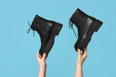 Mavi arka planda şık siyah deri çizmeleri olan kadın elleri.