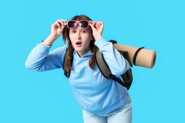 Mavi arka planda sırt çantalı ve güneş gözlüklü genç bir kadın. Seyahat kavramı