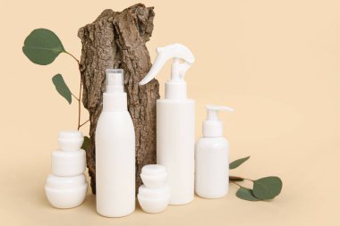 Kavanozlu kompozisyon, kozmetik ürünleri şişeleri, yeşil yapraklar ve bej arka planda ağaç kabuğu