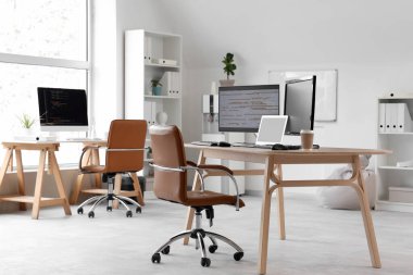 Ofisteki programcının masasında dizüstü bilgisayarlar ve kahve fincanları var.