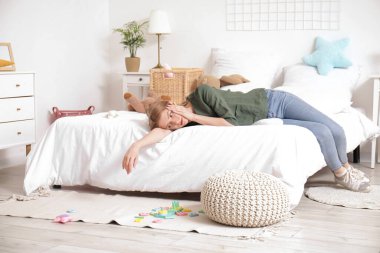 Yorgun genç anne yatak odasında dinleniyor dağınık oyuncaklarla