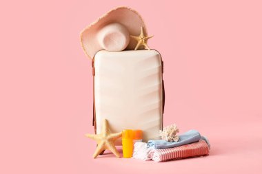 Çanta, plaj aksesuarları, güneş kremi ve pembe arka planda dekor.