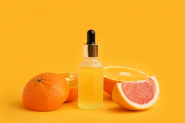 Bir şişe gerekli yağ ve renkli arkaplanda olgun turunçgil meyveleri.