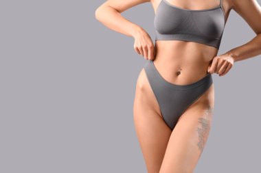 Beautiful young woman in grey underwear on light background