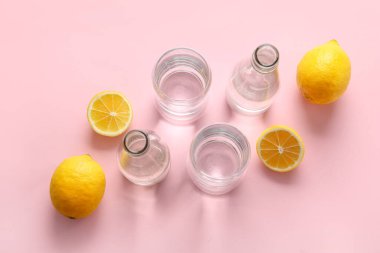 Temiz su şişeleri, pembe arka planda bardaklar ve limonlar