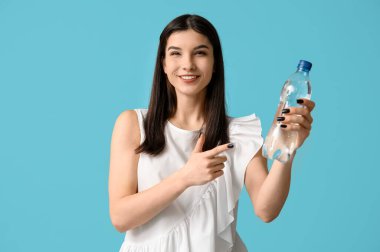 Genç Asyalı kadın mavi arka plandaki su şişesini işaret ediyor.