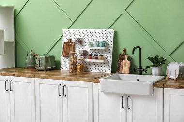 Mutfaktaki yeşil duvarın yanında tahta, yemek takımı ve ev bitkisi.