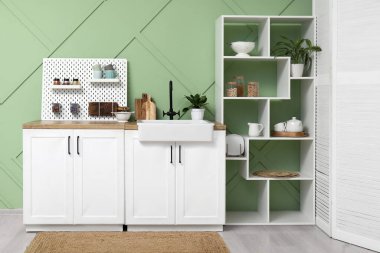 Tahta, beyaz tezgah ve askı modern mutfağın içindeki yeşil duvarın yanında.