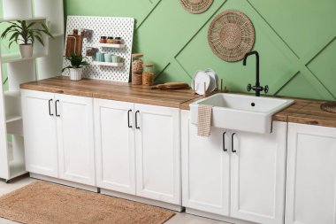 Beyaz tezgahlı, tahta tahtalı ve yeşil duvarlı şık bir mutfak.