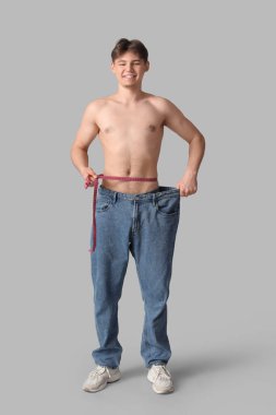 Gevşek kotlu ve gri arka planda şeritli genç bir adam. Diyet kavramı