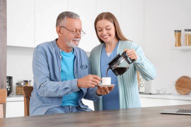 Hemşire mutfakta kıdemli bir adama kahve dolduruyor.