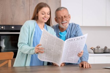 Hemşire ve kıdemli adam mutfakta gazete okuyorlar.