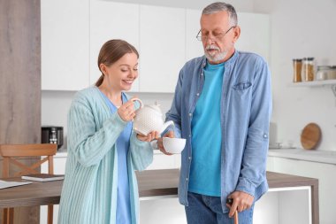 Hemşire mutfakta kıdemli bir adama çay dolduruyor.
