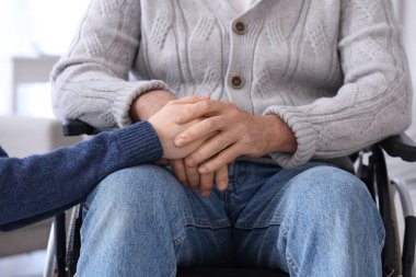 Tekerlekli sandalyedeki son sınıf öğrencisiyle bakımevinde el ele tutuşmuş, yakın plan.