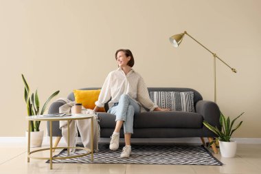 Genç, güzel bir kadın, oturma odasında, kanepede oturuyor.