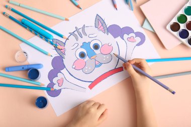 Kalemlerle, suluboya boyalarla ve bej arka planda farklı kırtasiyelerle çocuk eli çiziyor.