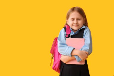 Sırt çantası ve sarı arka plan kitabı olan küçük tatlı bir kız öğrenci.