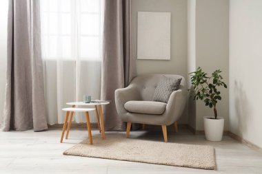 Interior of light living room with grey armchair and tables