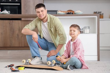 Young man and his little son fixing skateboard at home