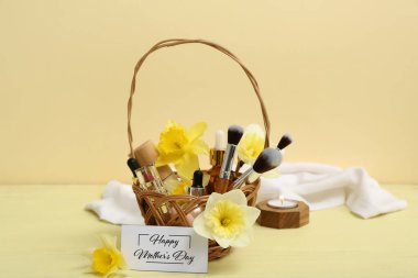 Kozmetik ürünlerle dolu hediye sepeti, makyaj fırçaları ve Anneler Günü için çiçekler renkli ahşap masada.