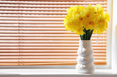 Lamba odasındaki pencere eşiğinde narsis çiçekleri olan vazo.