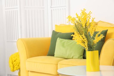 Oturma odasındaki masada sarı mimoza çiçekli vazo, yakın plan.