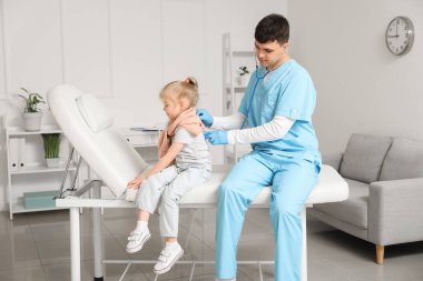 Erkek çocuk doktoru, klinikte steteskoplu küçük bir kızı muayene ediyor.