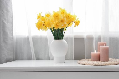 Masası, mumları ve narsisli çiçekleri olan şık bir oda.