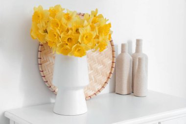 Beyaz odadaki masada narsist çiçekleri olan vazo.