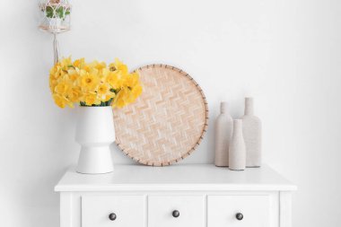 Beyaz odadaki masada narsist çiçekleri olan vazo.