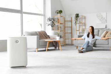 Modern nemlendirici ve genç bir kadın oturma odasında dinleniyor.