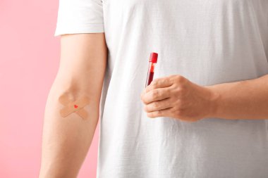 Uygulamalı tıbbi bantları olan kan bağışçısı ve pembe arka planda test tüpü, yakın plan.