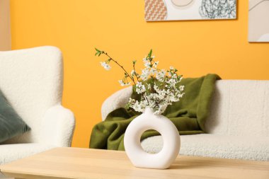 Oturma odasındaki portakal rengi duvarlı vazoda açan dallar.