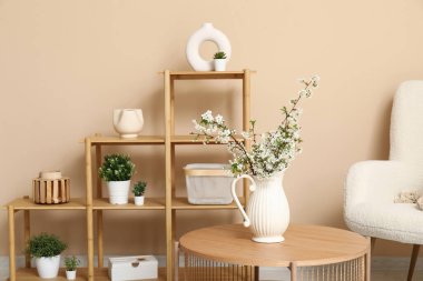 Koltuk, raf ve vazo, modern oturma odasının içindeki masanın üzerinde çiçek açan dallar.