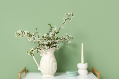 Çiçek açan dalları ve yeşil duvarın yanındaki masada mumu olan vazo.