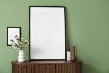 Boş çerçeve ve çiçek açan dallar yeşil duvarın yanındaki ahşap çekmece sandığında.