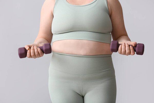 Толстая женщина с гантелями на светлом фоне. Концепция потери веса