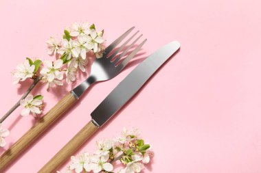 Pembe arka planda çiçek açan dalları olan gümüş çatal bıçak takımı.