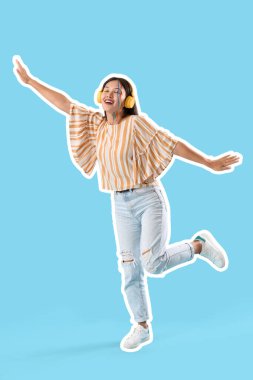 Mavi arka planda dans eden yüzü boyalı ve kulaklıklı mutlu Asyalı kadın.