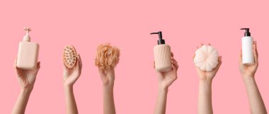 Pembe arka planda farklı banyo malzemelerine sahip kadın elleri.