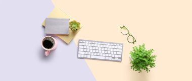 Modern bilgisayar klavyesi, bir fincan kahve, gözlük, ev bitkileri ve gri ve bej arka plan üzerine not defterleri.