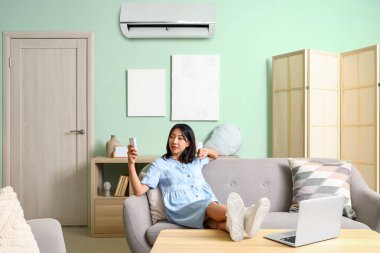 Güzel Asyalı kadın evde klimayı açıyor.